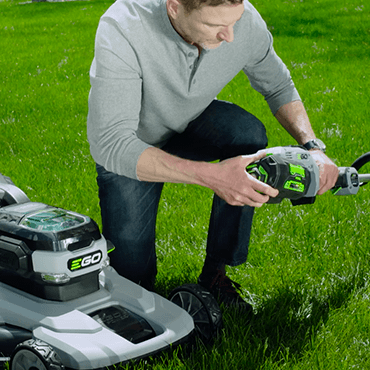 Man swapping EGO battery from EGO lawn mower to  EGO string trimmer.